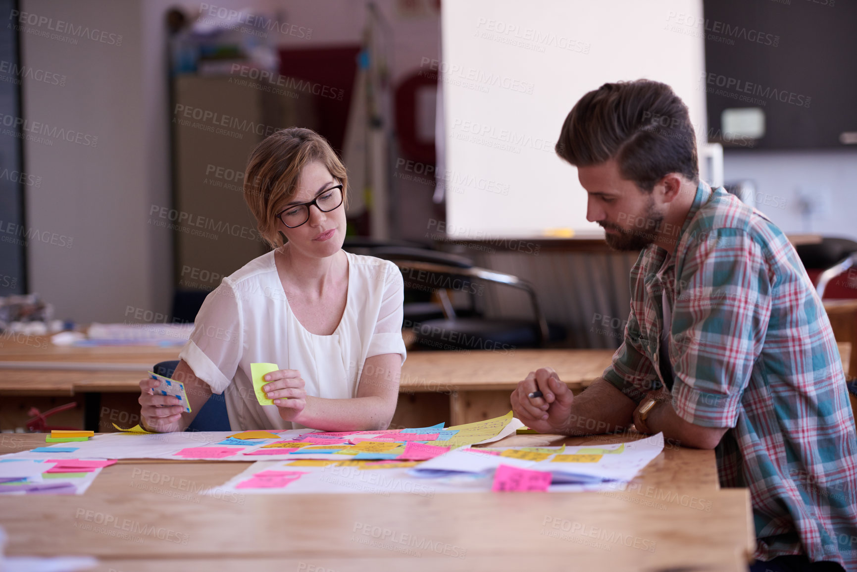 Buy stock photo A young woman looking at sticky notes on the desk in her office