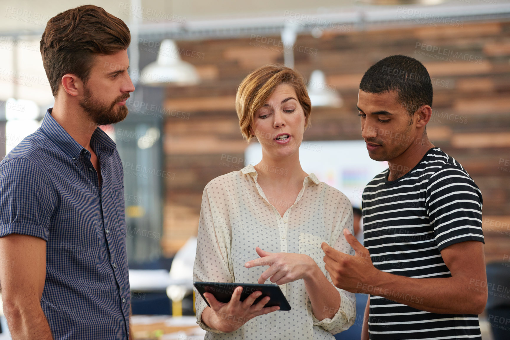 Buy stock photo Shot of three colleagues using a digital tablet together in a casual working environment