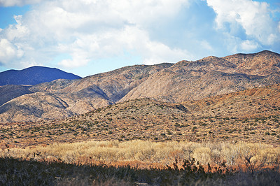 Buy stock photo Landscape, sustainable and mountains in nature for agriculture, eco friendly and agro environment. Outdoor, travel and dry habitat with grass, blue sky and clouds for natural hiking trail by rocks.