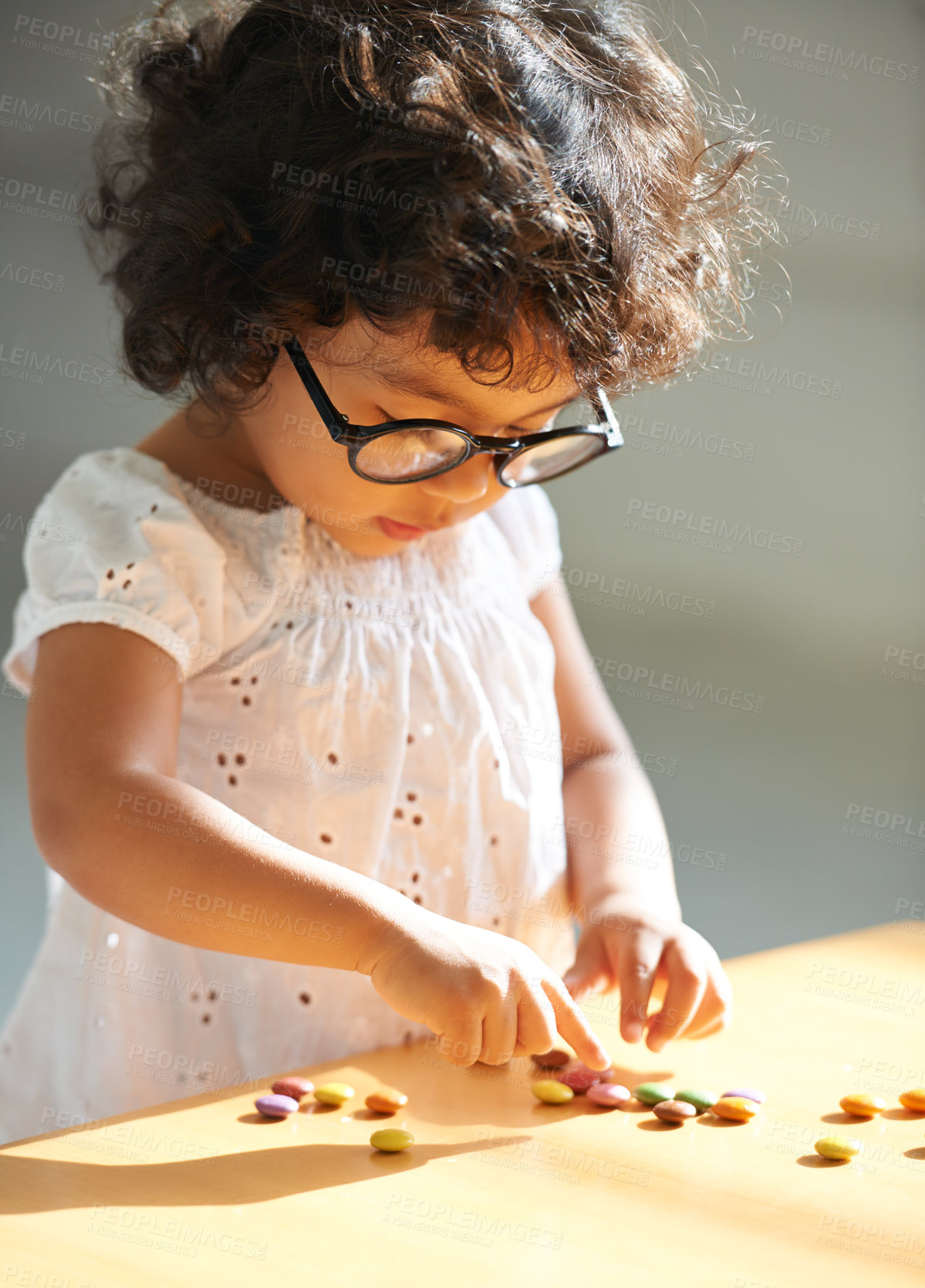 Buy stock photo Toddler, counting and sweets for learning math, equation or childhood development knowledge. Girl, glasses and candy  on table for intelligence growth or education homework, preschool or study reward