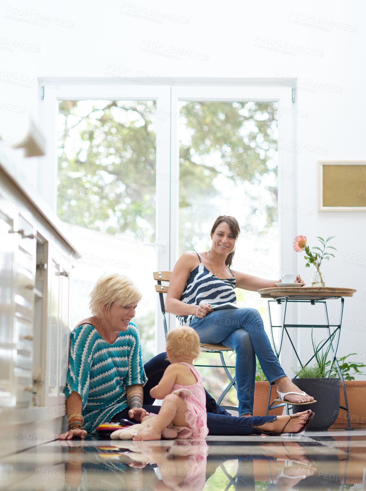 Buy stock photo Shot of a happy lesbian couple relaxing with their daughter in a kitchen