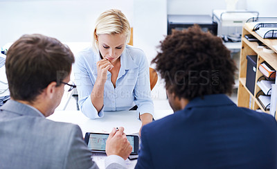 Buy stock photo Shot of a serious businesswoman looking at information presented to her by colleagues
