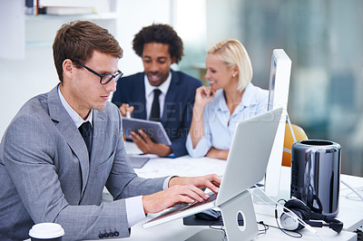 Buy stock photo Shot of a businessman working on his laptop with colleagues in the background