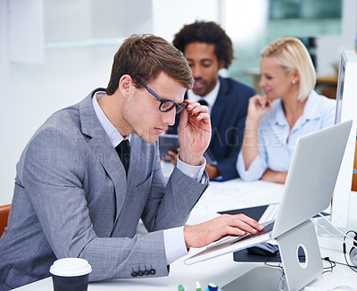 Buy stock photo Shot of a businessman looking carefully at his laptop with colleagues in the background