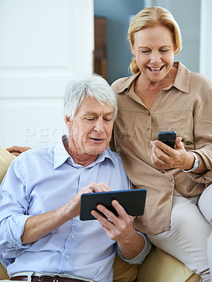 Buy stock photo Shot of a happy elderly man using a digital tablet while his wife reads a text message on her cellphone