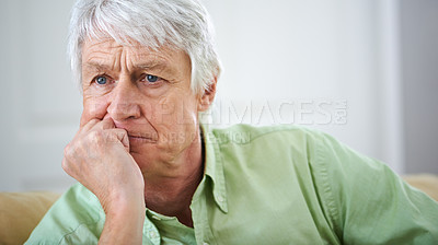 Buy stock photo A sad senior man at home, sitting on a sofa in the living room. Worried older male concerned about pension and retirement. Mature man alone in his house, in mourning after death of his spouse