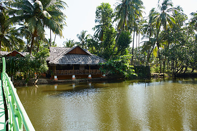 Buy stock photo Traditional wooden building surrounded by tropical palm trees on the banks of a river in India  