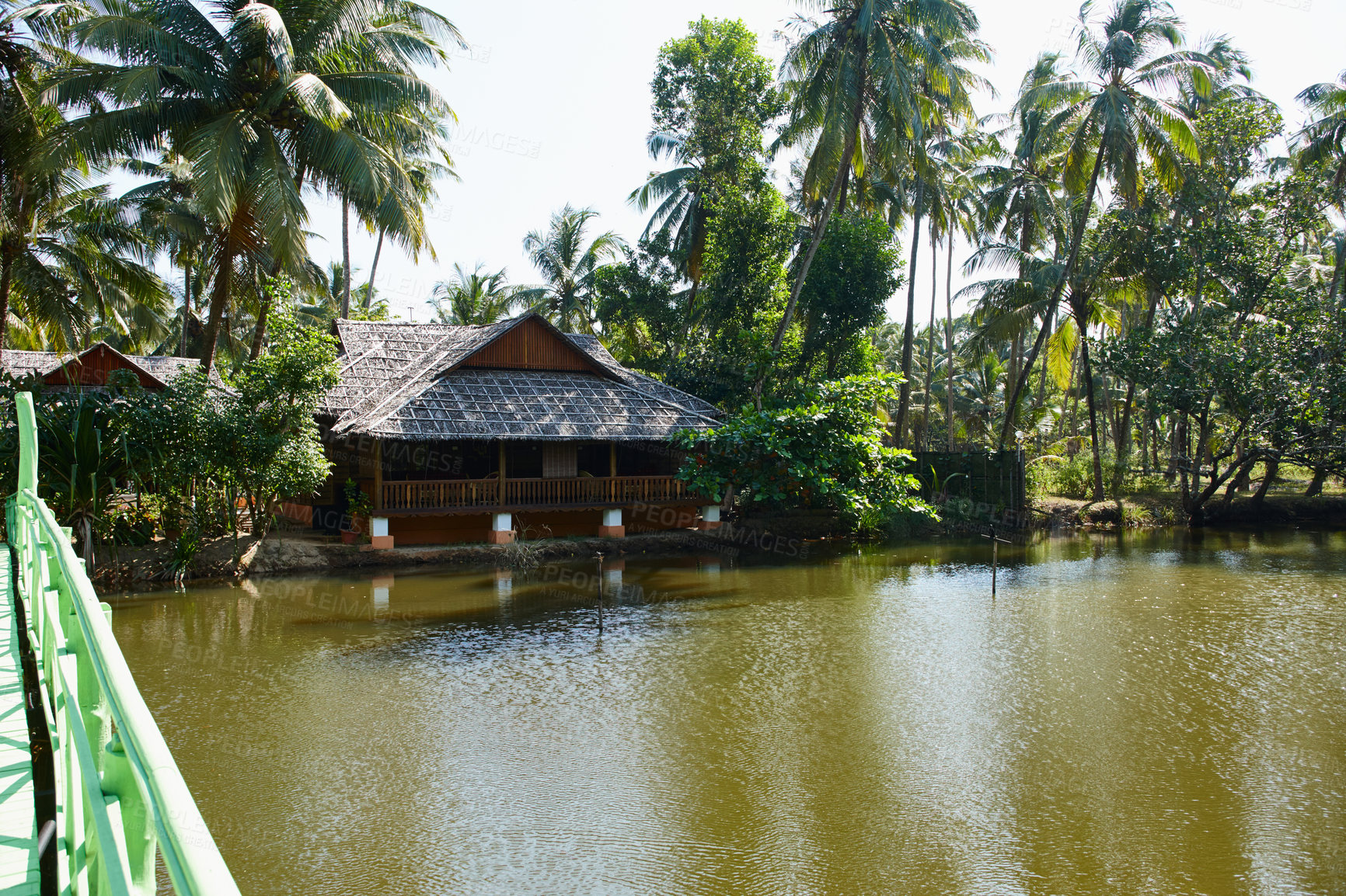 Buy stock photo Traditional wooden building surrounded by tropical palm trees on the banks of a river in India  