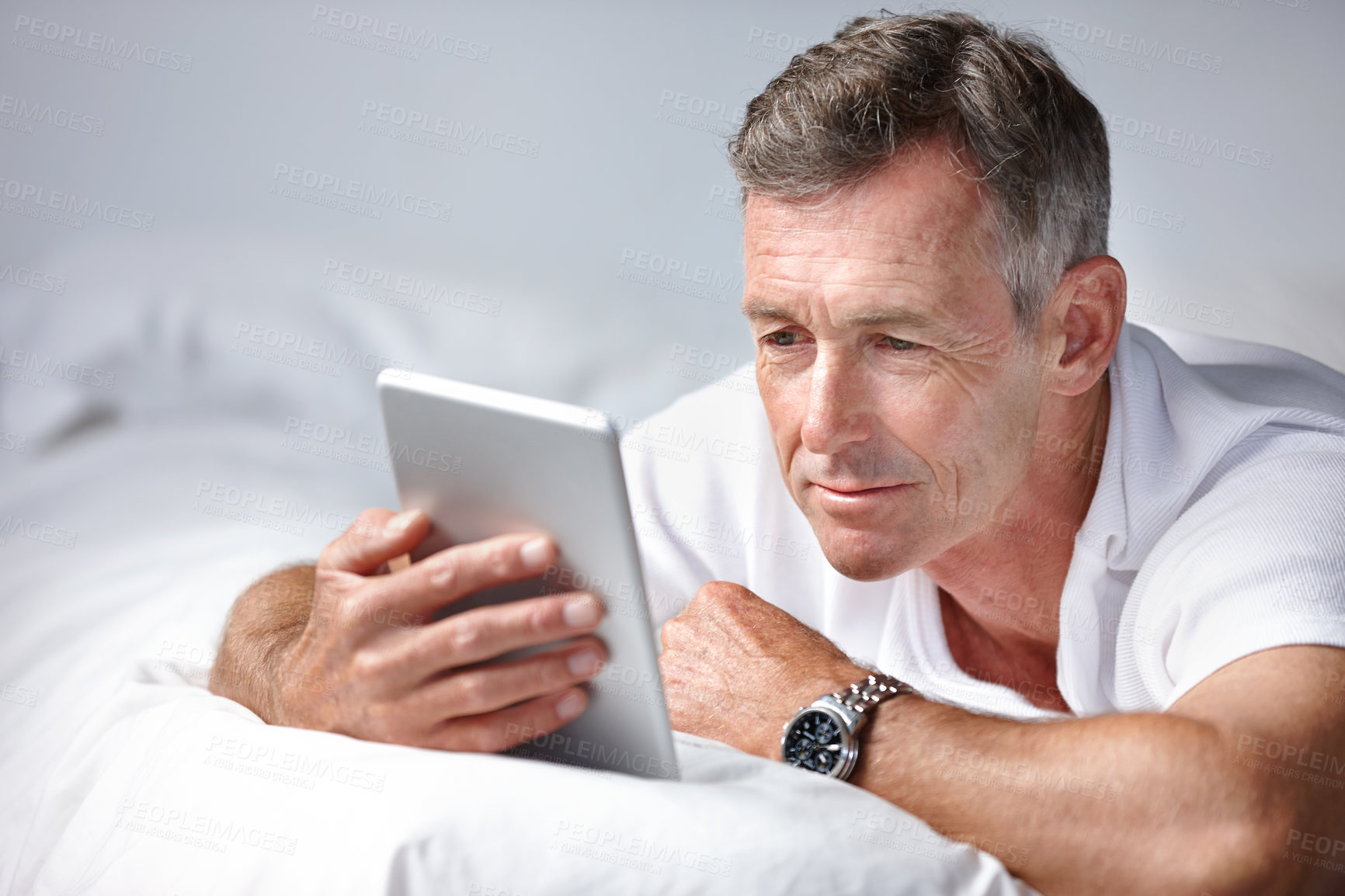 Buy stock photo Shot of a mature man using a digital tablet while lying on his bed