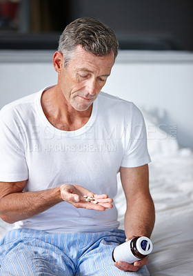 Buy stock photo Shot of a serious mature man sitting on a bed with his medication