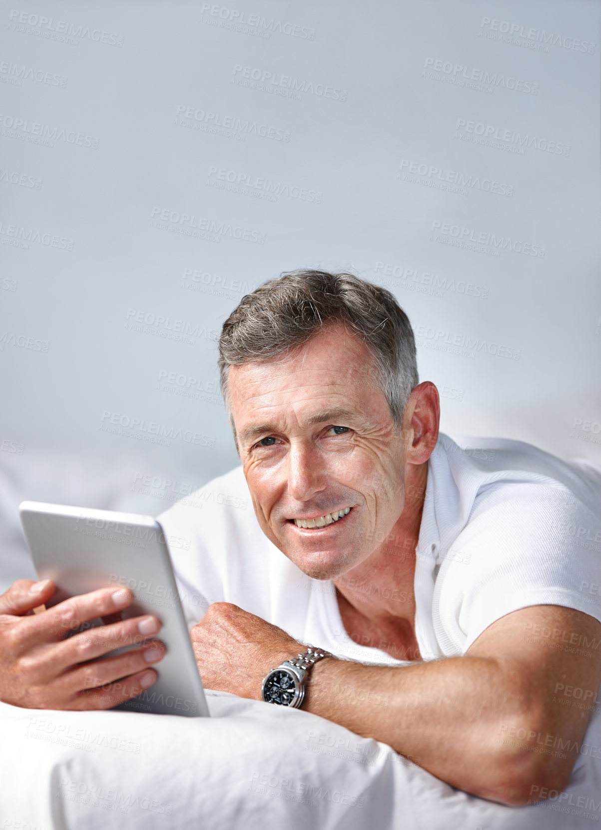 Buy stock photo Shot of a mature man using a digital tablet while lying on his bed