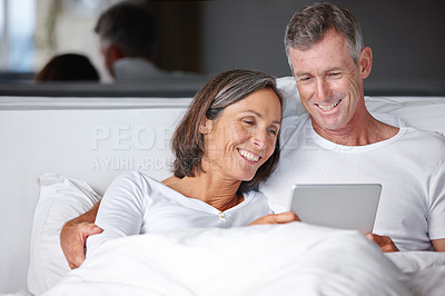 Buy stock photo Shot of a happy mature couple sitting in bed with a digital tablet