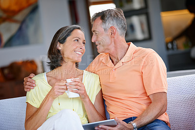 Buy stock photo Shot of a loving mature couple sitting on a sofa with coffee and a digital tablet