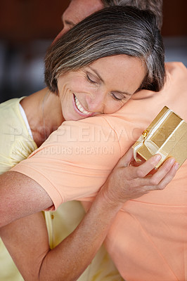 Buy stock photo Shot of an attractive mature woman hugging her husband after receiving a gift from him