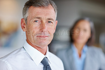 Buy stock photo Portrait of a mature businessman with his colleague standing in the background