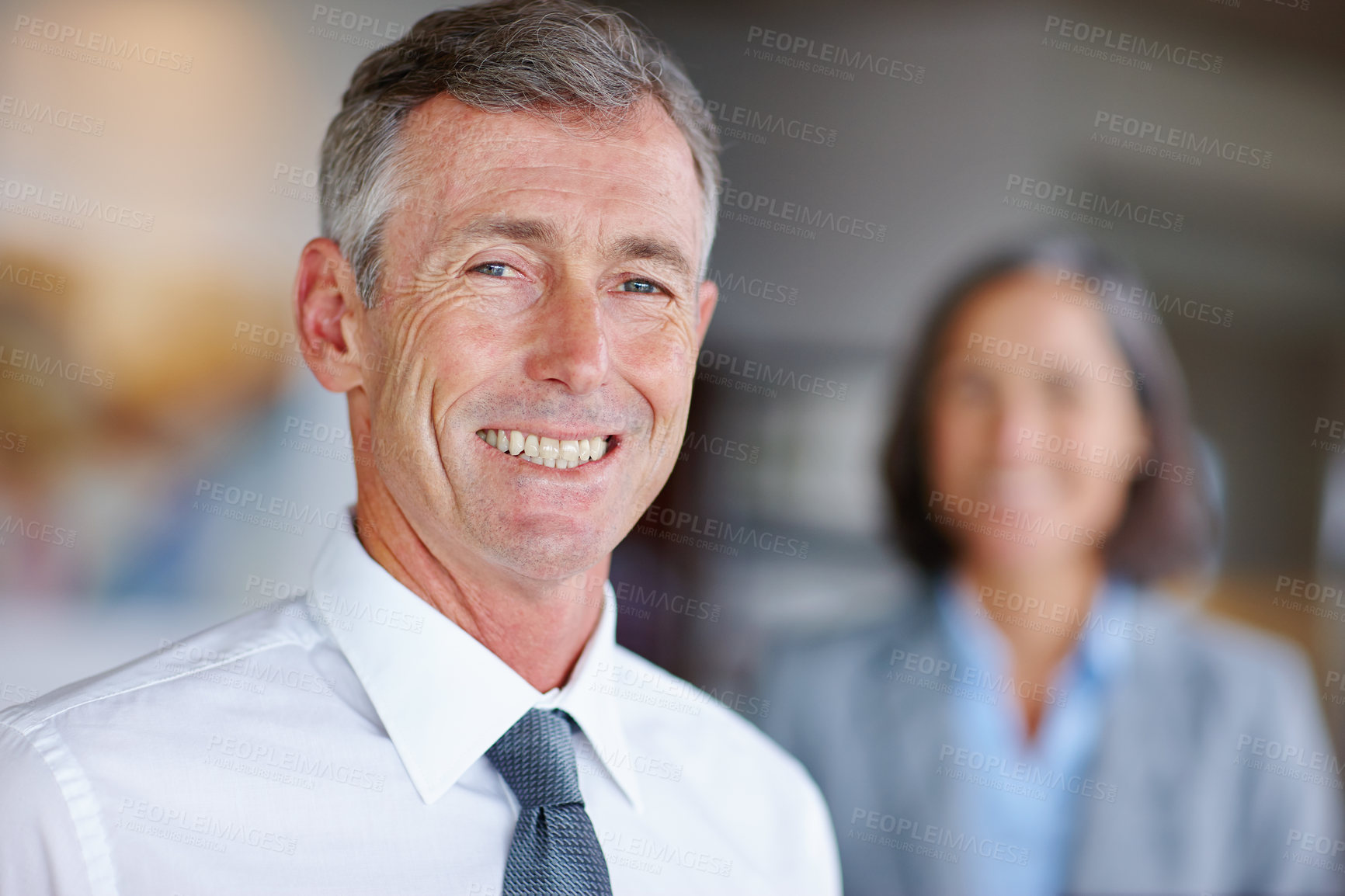 Buy stock photo Portrait of a mature businessman with his colleague standing in the background