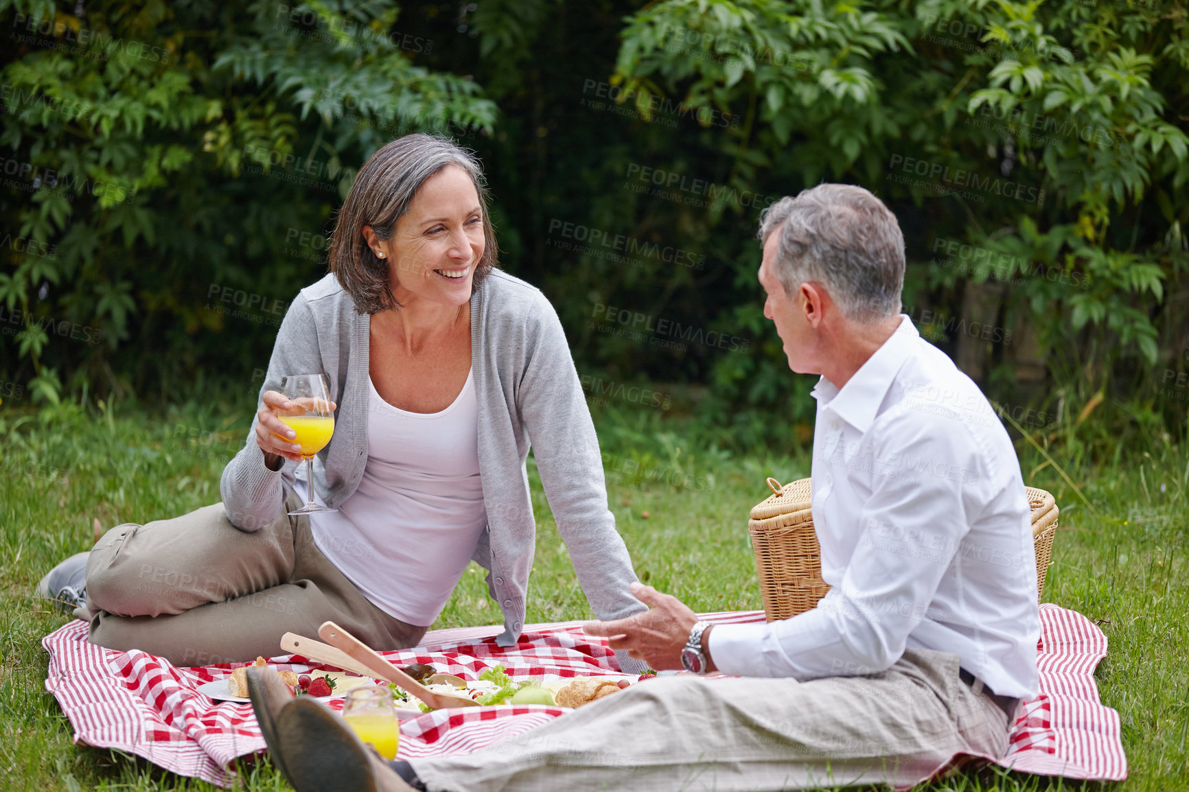 Buy stock photo Park, mature couple and picnic with food for nutrition, hungry and bonding together with communication. Happy people, man and woman with juice glass for drinking, beverage and commitment in marriage