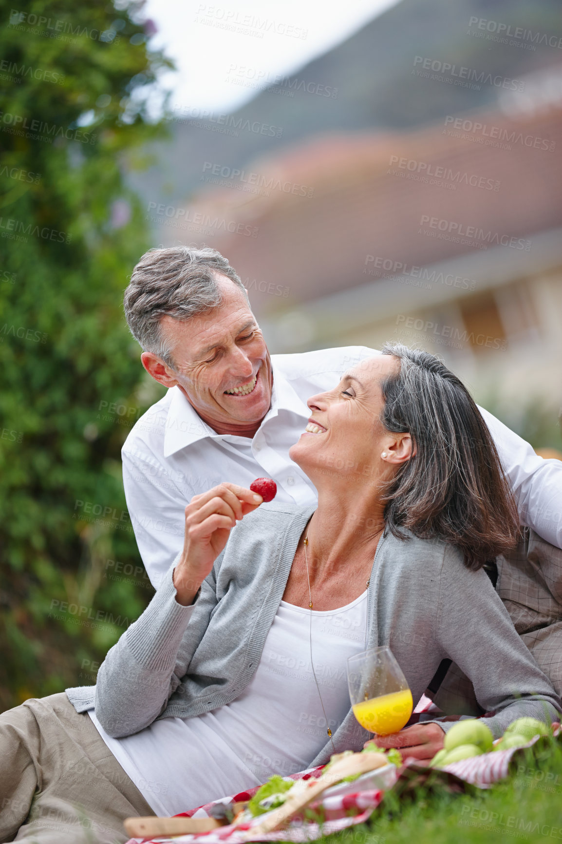 Buy stock photo Mature, couple and eating on picnic outdoor with healthy fruit, bonding together and food basket of romantic date. People, laugh and love with juice of relationship anniversary, commitment and nature