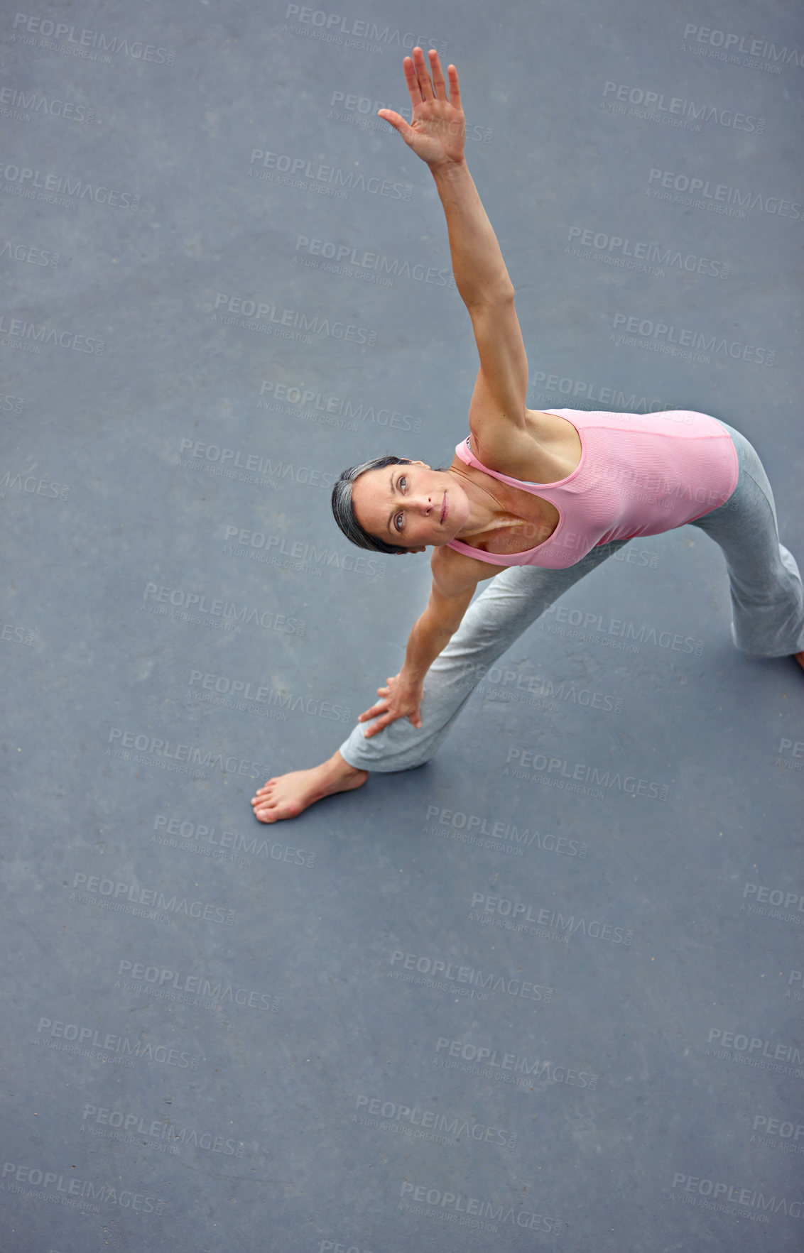 Buy stock photo Shot of a mature woman doing the extended triangle yoga pose outdoors