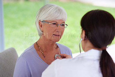 Buy stock photo Shot of a senior woman looking seriously at her doctor while having her heart checked out