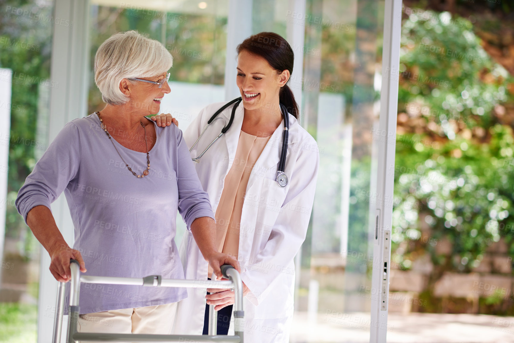 Buy stock photo Shot of a senior woman using an orthopedic walker, chatting happily with her doctor