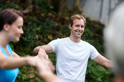 Buy stock photo Male yoga coach holding hands with group of people during meditation. Fitness yogi or training instructor smiling while standing in a circle outside a yoga exercise class or fitness retreat weekend