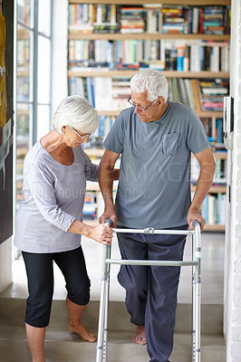 Buy stock photo Shot of a senior woman assisting her husband who's using a walker for support