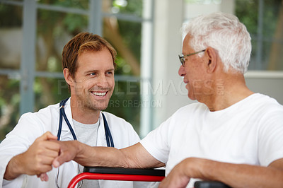 Buy stock photo Shot of a handsome male doctor talking to his senior patient who's in a wheelchair