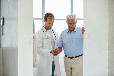 Buy stock photo Shot of a male doctor supporting his senior patient as he's walking