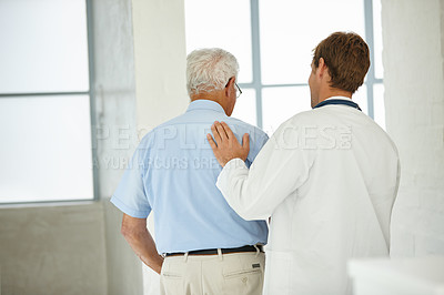 Buy stock photo Rearview shot of a male doctor supporting his senior patient as he's walking