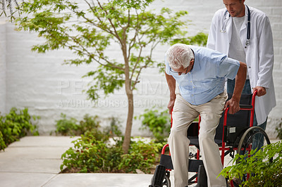 Buy stock photo Shot of a male doctor helping his senior patient into a wheelchair outside