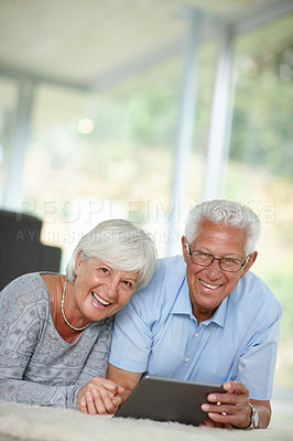 Buy stock photo Shot of a senior couple lying on the floor while using a digital tablet