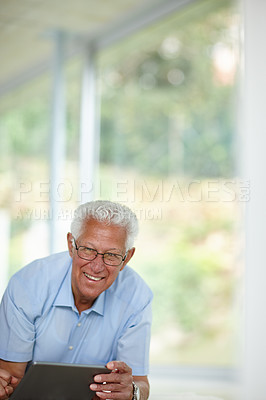 Buy stock photo Shot of a senior man using his digital tablet at home