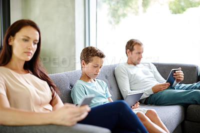 Buy stock photo Shot of a family of three sitting separately on a sofa with their own digital devices