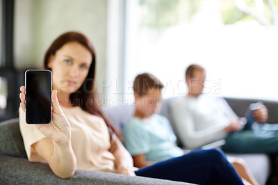 Buy stock photo Shot of a woman holding up a smartphone while her family are busy on their own devices