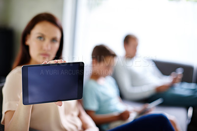 Buy stock photo Shot of a woman holding up a tablet while her family are busy on their own devices