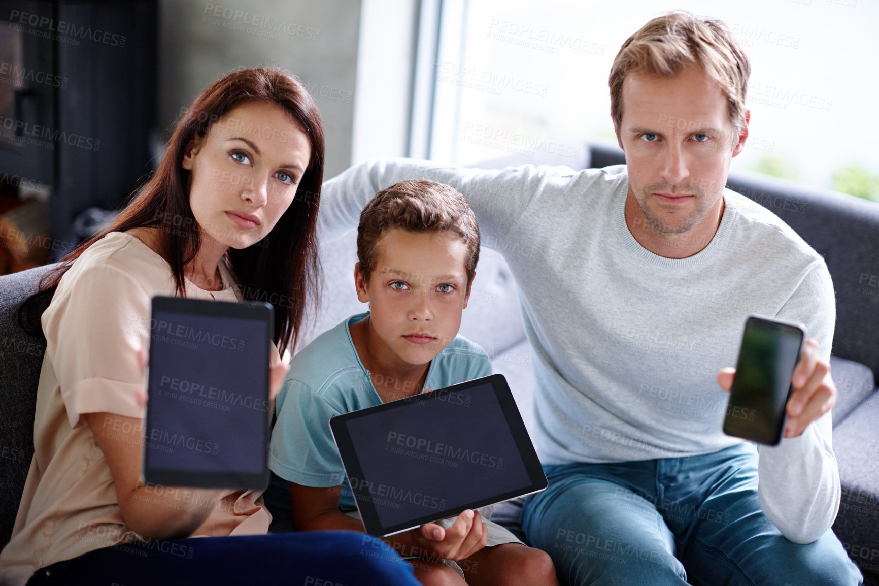 Buy stock photo Portrait of a family looking serious as they hold up their digital devices