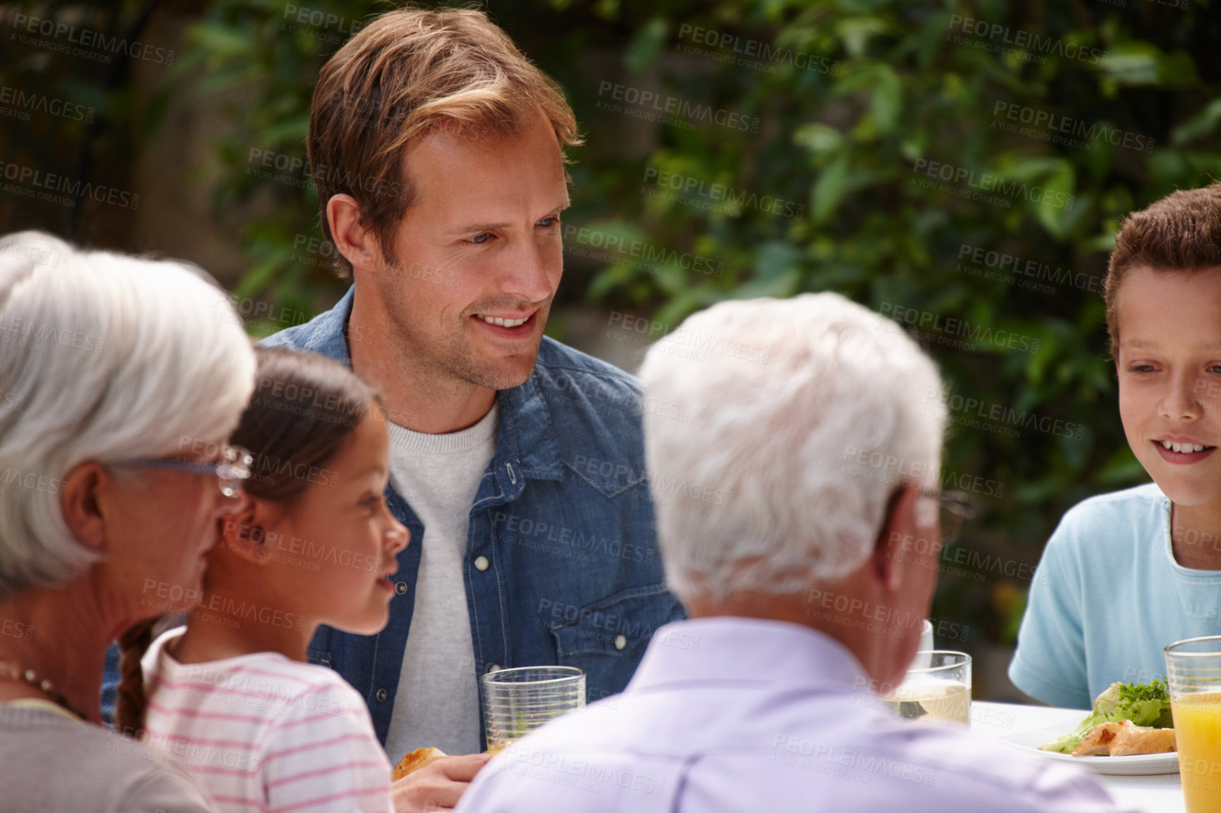 Buy stock photo Shot of a happy multi-generational family having a meal together outside