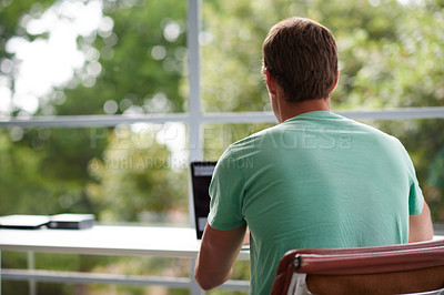 Buy stock photo Rearview shot of a young man using a laptop at home
