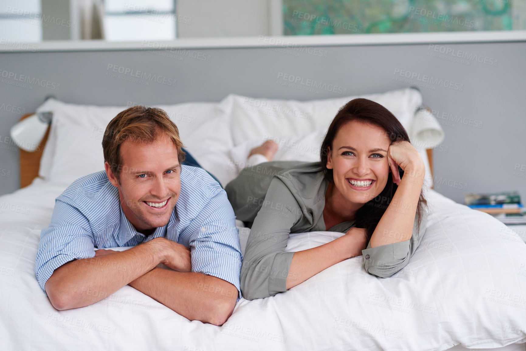 Buy stock photo Portrait of a happy young couple lying on their bed at home