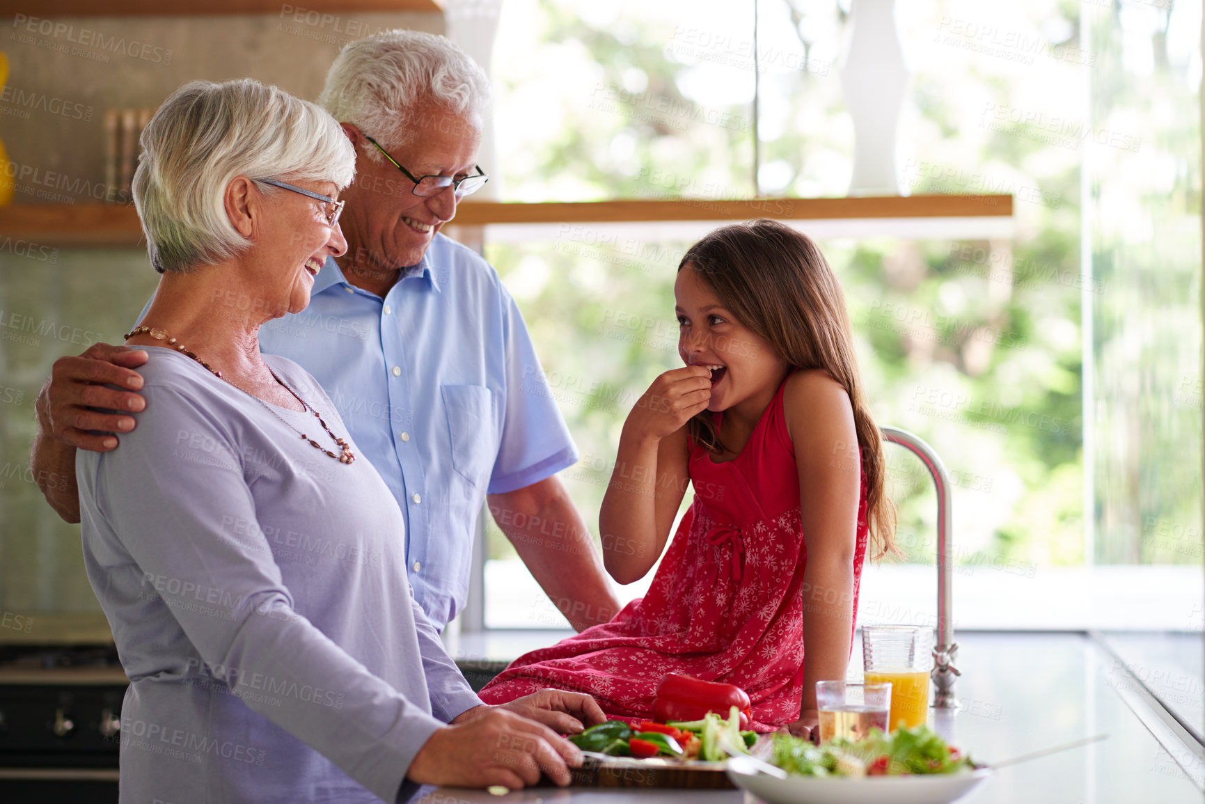 Buy stock photo Grandparents, girl and cooking in kitchen, happy and taste with bonding, love and relax together in family house. Senior man, woman and child with eating, salad and laughing at funny joke in home