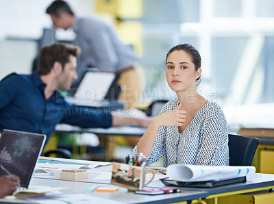 Buy stock photo Portrait of a young office worker at her desk with colleagues in the background