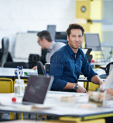 Buy stock photo Portrait of a young office worker at his desk with colleagues in the background