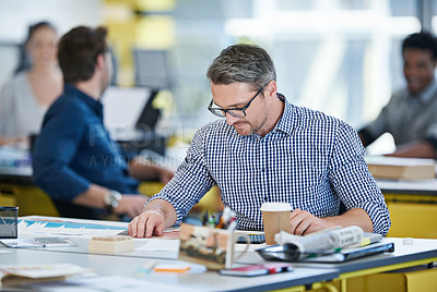Buy stock photo Shot of an office worker sitting at his desk with colleagues in the background