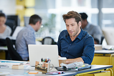 Buy stock photo Portrait of a designer sitting at his desk working on a laptop with colleagues in the background