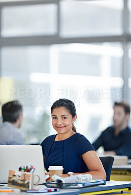 Buy stock photo Portrait of a designer sitting at her desk working on a laptop with colleagues in the background