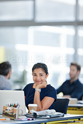 Buy stock photo Portrait of a designer sitting at her desk working on a laptop with colleagues in the background