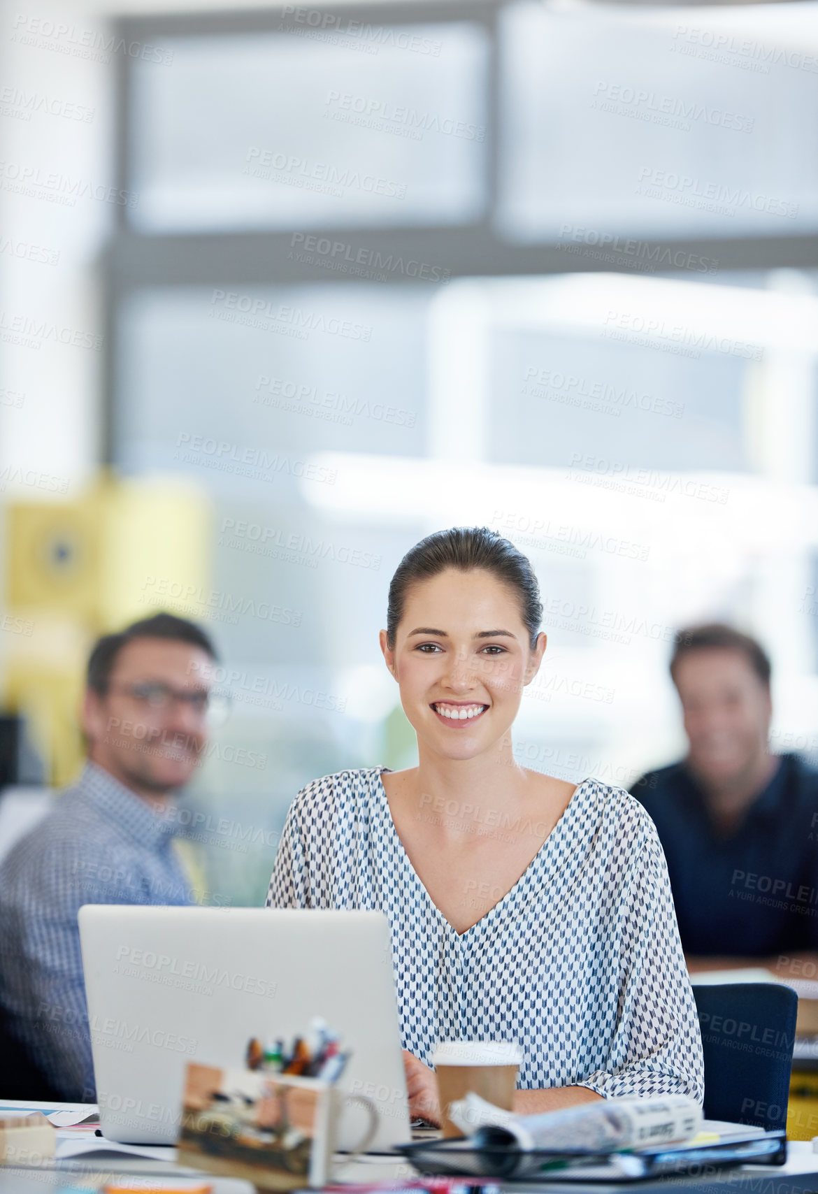 Buy stock photo Portrait of a designer sitting at her desk working on a laptop with colleagues in the background