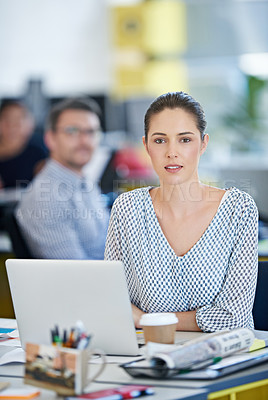 Buy stock photo Portrait of a designer sitting at her desk working on a laptop with colleagues in the background