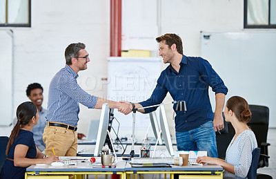 Buy stock photo Shot of two designers shaking hands over their computers in an office